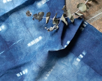 May include: A blue fabric with a white tie-dye pattern. The fabric is folded and a branch of dried eucalyptus leaves is placed on top.