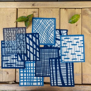 Op de afbeelding: Een verzameling van acht blauwe en witte vierkante stoffen met verschillende geometrische patronen. De vierkanten zijn willekeurig gerangschikt op een houten oppervlak.