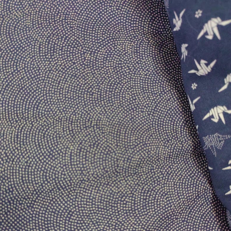 May include: A close-up of a dark blue fabric with a white pattern of small dots arranged in a wave-like design. The fabric is textured and has a subtle sheen.