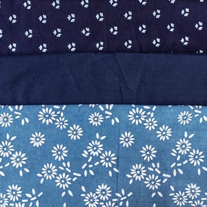 May include: Three pieces of fabric, one dark blue with a white pattern, one solid dark blue, and one light blue with a white floral pattern.
