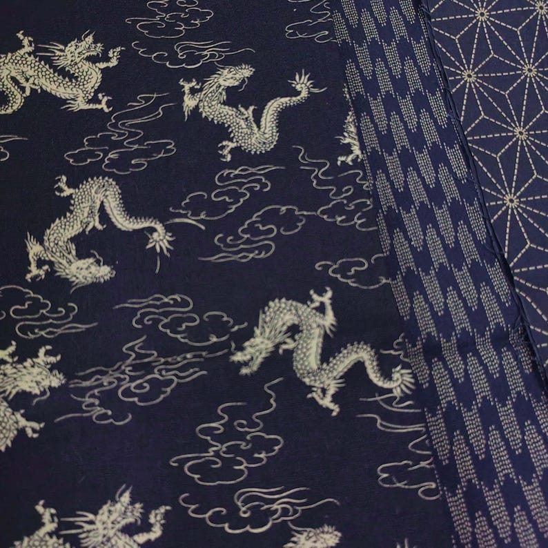 May include: A dark blue fabric with a white dragon pattern. The fabric has a repeating pattern of dragons flying through clouds. The fabric is bordered by a white and blue geometric pattern.