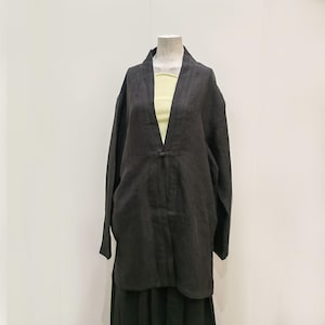 Könnte beinhalten: Schwarze Leinenjacke mit V-Ausschnitt und langen Ärmeln. Die Jacke hat einen einzelnen Knopfverschluss und wird auf einer Schaufensterpuppe präsentiert. Ein hellgelbes Oberteil ist darunter sichtbar.