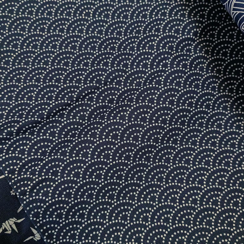 May include: A close-up of a dark blue fabric with a white pattern of small circles arranged in a wave-like design.
