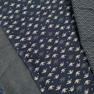 May include: Two pieces of dark blue fabric with white patterns. One fabric has a repeating pattern of origami cranes. The other fabric has a repeating pattern of small white dots.