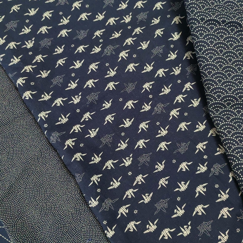 May include: Two pieces of dark blue fabric with white patterns. One fabric has a repeating pattern of origami cranes. The other fabric has a repeating pattern of small white dots.