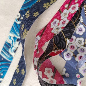 May include: Four different fabric ribbons with various patterns. The ribbons are blue, black, pink, and white with floral and wave designs.