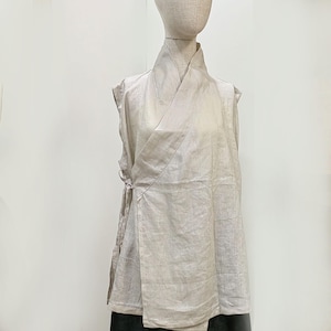 Peut inclure: Haut sans manches de couleur beige clair, de style cache-cœur. Il présente un col haut replié et une fermeture à nouer sur le côté. Le tissu semble léger et légèrement brillant, peut-être du lin. Le vêtement est présenté sur un mannequin.