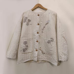 May include: A white quilted jacket with a button-up front and a floral print. The jacket has two pockets on the front.