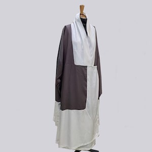 May include: A two-tone robe displayed on a mannequin. The robe features a dark brown panel on the left side and a white panel on the right side. A white shawl-like collar drapes over the shoulders. The robe is floor-length.