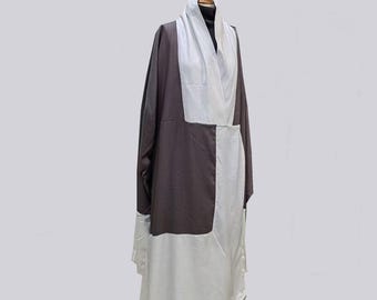 Pode incluir: Um robe de duas cores exibido em um manequim. O robe apresenta um painel marrom escuro no lado esquerdo e um painel branco no lado direito. Uma gola tipo xale branca drapeja sobre os ombros. O robe é longo.
