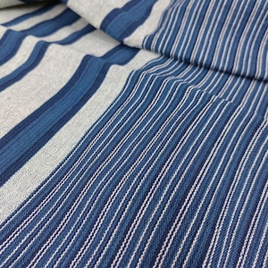 May include: Close-up of a blue and white striped fabric. The fabric has a woven texture and is made of cotton.