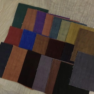May include: A selection of fabric swatches in a range of colours, such as green, blue, brown, and purple. The squares are arranged in a layered pattern, displaying the different textures and hues of the materials. The swatches are likely for textile or design projects.