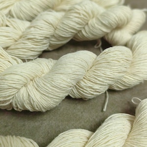 Pode incluir: Um close-up de um novelo de fio de algodão branco natural. O fio é macio e felpudo, e é perfeito para tricotar ou fazer crochê.