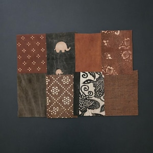 May include: A collection of eight rectangular fabric swatches arranged in a grid. The patterns include brown with white floral motifs, black with light-coloured elephant silhouettes, solid brown, brown with white floral prints, solid dark grey, brown with white geometric shapes, black and white floral designs, and a brown grid pattern.