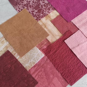 May include: A collection of square fabric swatches in various shades of red, pink, and tan. The pieces feature diverse textures, including smooth, crinkled, and woven surfaces, with some displaying intricate floral and geometric patterns.