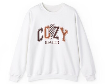 May include: White sweatshirt with the word "COZY" in brown and orange block letters, with a checkered lightning bolt in the center. The word "SEASON" is below the word "COZY".