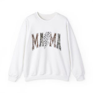 May include: White sweatshirt with the word "MAMA" in a brown, black, and white checkered lightning bolt design. The sweatshirt has a crew neck and long sleeves.