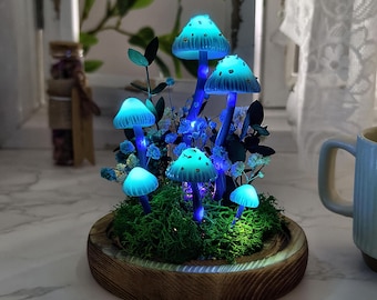 Puede incluir: Una base de madera con musgo y un grupo de setas azules brillantes. Las setas están dispuestas de forma caprichosa con algunas ramitas de flores secas.