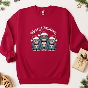May include: A red sweatshirt with a graphic of three blue monkeys wearing Santa hats, and the words "Merry Christmas" in white script. A festive Christmas-themed garment.