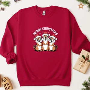 May include: A red sweatshirt with a graphic of three cartoon chipmunks wearing Santa hats, and the words "MERRY CHRISTMAS" above them. The sweatshirt is a solid red colour.