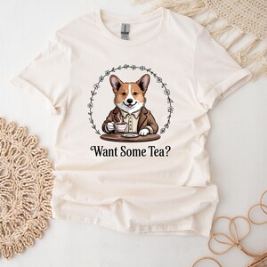 May include: A white t-shirt featuring a cartoon image of a corgi dog wearing a brown jacket and holding a teacup. The text "Want Some Tea?" is printed below the image.