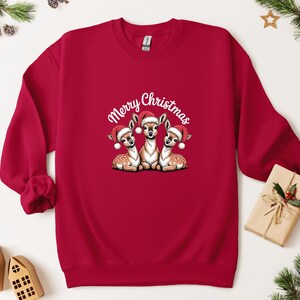 May include: A crimson red sweatshirt featuring a graphic of three deer wearing Santa hats, with the words "Merry Christmas" in white script. A festive Christmas jumper.