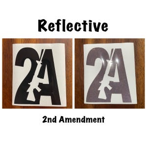 以下が含まれることがあります： 「2A」の数字と「A」の中にライフルのシルエットが入った、黒と白の反射ステッカー2枚。「2nd Amendment」というテキストがステッカーの下にあります。