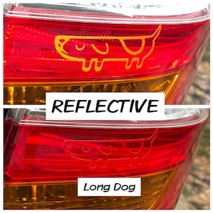 Könnte beinhalten: Ein rotes Rücklicht eines Autos mit einem reflektierenden gelben Aufkleber eines langen Hundes mit dem Text "REFLECTIVE" und "Long Dog" auf dem Aufkleber.