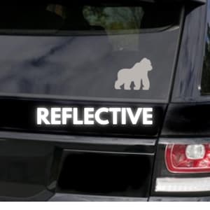 May include: A black car with a white reflective sticker that says "REFLECTIVE" and a white silhouette of a gorilla on the back window.