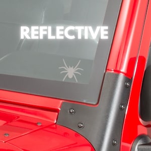 May include: A red car with a black spider decal on the back window. The decal is reflective and says "REFLECTIVE" in white letters.