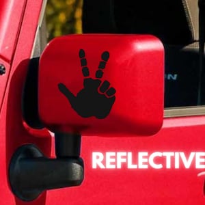 May include: A red car side mirror with a black hand making a peace sign sticker. The sticker says "REFLECTIVE" in white letters.