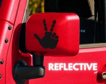 May include: A red car side mirror with a black hand making a peace sign sticker. The sticker says "REFLECTIVE" in white letters.
