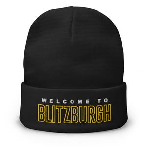 May include: Black beanie with the text "WELCOME TO BLITZBURGH" in white and gold. The hat is a winter accessory, perfect for cold weather. The text is embroidered on the folded brim.
