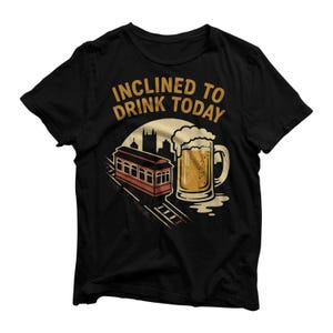 Könnte beinhalten: Schwarzes T-Shirt mit einem Grafikdesign, das eine Straßenbahn, einen großen Bierkrug und den Text "INCLINED TO DRINK TODAY" in goldfarbenen Buchstaben zeigt. Das Design beinhaltet eine Stadtsilhouette und eine Sonne.