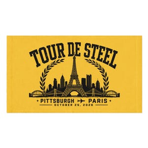 Peut inclure: Une serviette rectangulaire jaune avec une impression graphique noire. Le texte indique TOUR DE STEEL, PITTSBURGH, PARIS et OCTOBER 25, 2026. Le motif comprend une tour Eiffel centrale, une ligne d'horizon, des lauriers et un avion.