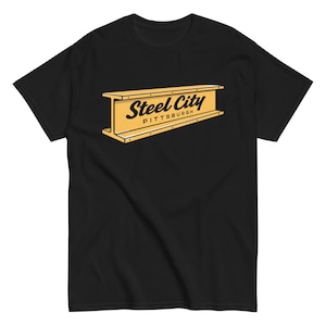 May include: Black t-shirt featuring a yellow and black graphic of a steel beam with the words "Steel City Pittsburgh" in a stylized font. The shirt is a short-sleeved crew neck.