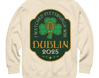 May include: Cream-colored sweatshirt with a green and gold graphic. The graphic features a shamrock with a football in the center, and the text "I WATCHED PITTSBURGH WIN DUBLIN 2025".
