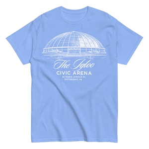 以下が含まれることがあります： 白いドーム型の建物のグラフィックと「The Igloo CIVIC ARENA 66 MARIO LEMIEUX PL PITTSBURGH, PA」の文字が入った、水色のTシャツ。柔らかい素材で作られています。