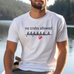 Puede incluir: Camiseta blanca con el texto "no crabs allowed" y un gráfico de un equipo de remo con un cangrejo debajo del bote.