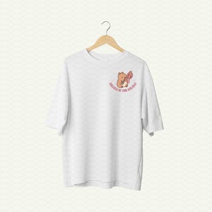 May include: White t-shirt with a brown bear holding a pink flower and the text "Honey in the Wild" printed on the front.
