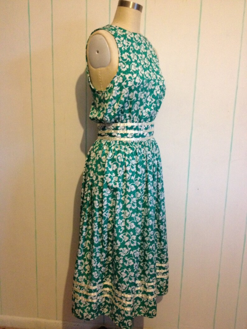 May include: A green and white floral print dress with a white trim around the neckline and hem. The dress has a fitted bodice and a full skirt.