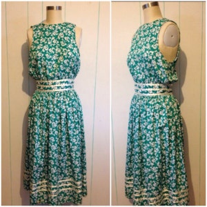 May include: A sleeveless green and white floral dress with a white ribbon around the waist. The dress has a white trim around the bottom.