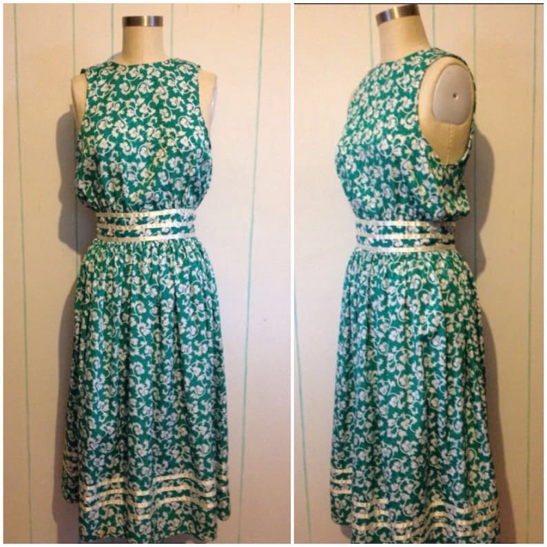 May include: A sleeveless green and white floral dress with a white ribbon around the waist. The dress has a white trim around the bottom.