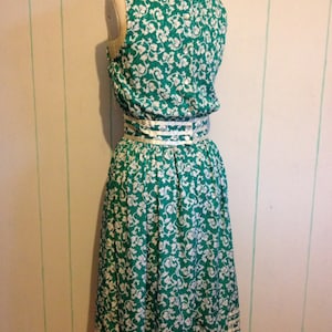 May include: A green and white floral print dress with a white ribbon belt and white trim around the bottom hem.