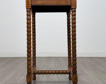 May include: A small, antique wooden side table with a rectangular top and turned legs. The table is made of a warm-toned wood, with a dark finish. The legs are intricately carved with a bobbin design. The table is a classic piece of furniture.