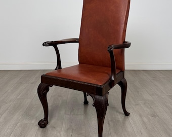 May include: A dark brown wooden armchair with a high back and armrests. The seat and back are upholstered in reddish-brown leather. The chair has carved details and claw feet, showcasing a classic design.