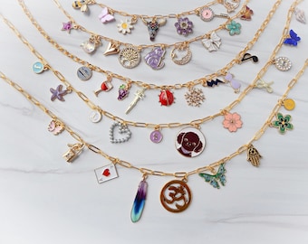 May include: A set of gold chains with various charms, including a butterfly, a heart, a wine glass, a flower, a snowflake, a ladybug, a musical note, a star, a hand, a feather, a dog, a tree, a crescent moon, a letter 'J', a letter 'S', a letter 'L', a padlock, a playing card, and an Om symbol.