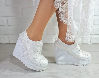 May include: White lace wedge platform shoes with a white lace trim. The shoes have a white sole and a white lace design on the front.