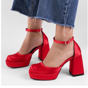 Peut inclure: Chaussures à talons hauts plateforme en satin rouge avec des brides à la cheville. Les talons mesurent environ 10 cm de haut et ont une plateforme épaisse.