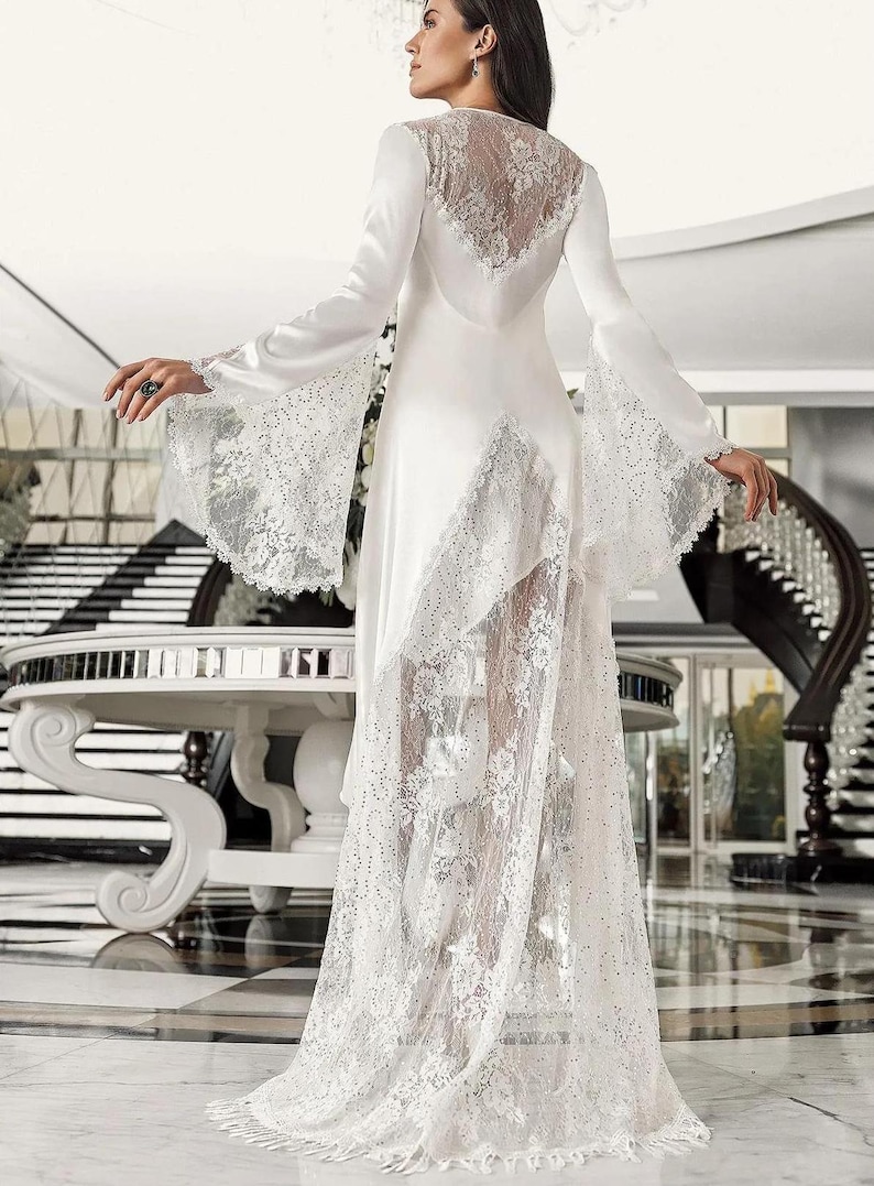 May include: A white satin and lace gown with long sleeves and a flowing skirt. The gown has a sheer lace overlay and a V-neckline.